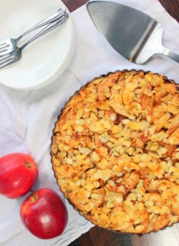 Apple pie topped with sliced almonds in tart pan.