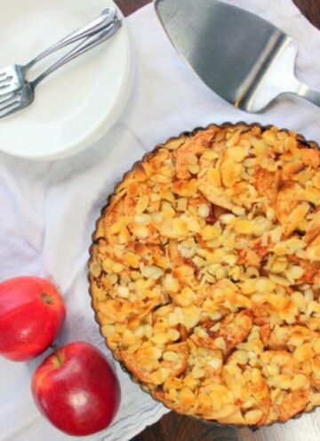 Apple pie topped with sliced almonds in tart pan.