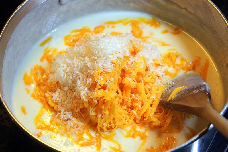 Cheddar and parmesan cheese in white sauce in metal pot on stove.