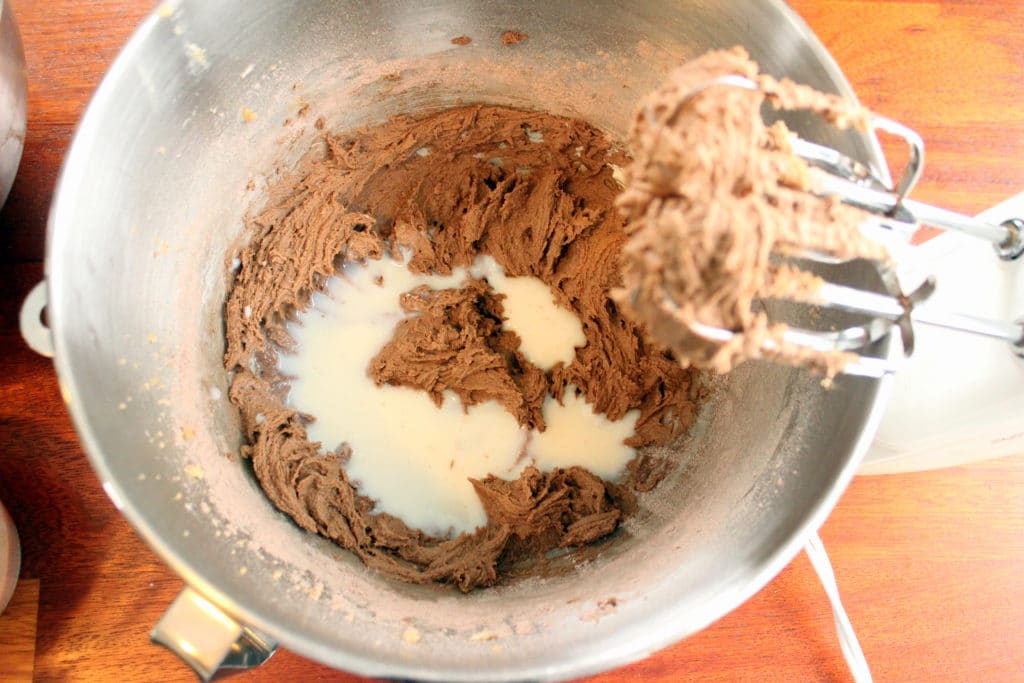Milk on top of chocolate mixture in metal mixing bowl.