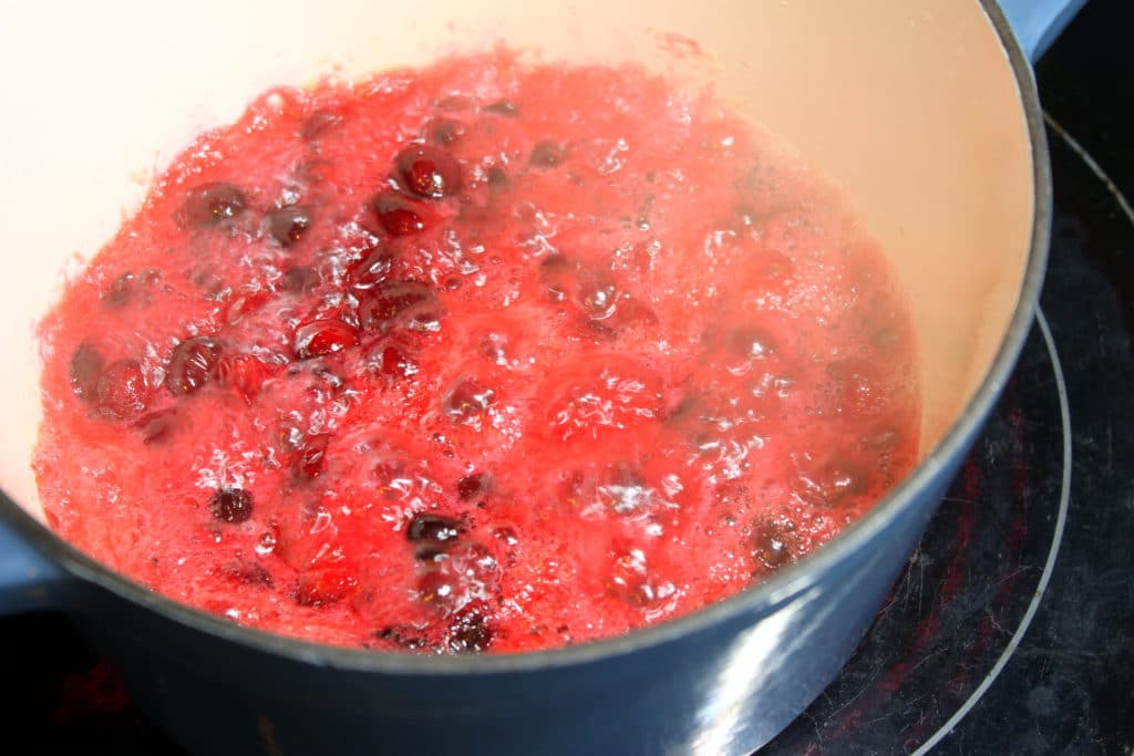 Cranberries in blue pot boiling on stove.