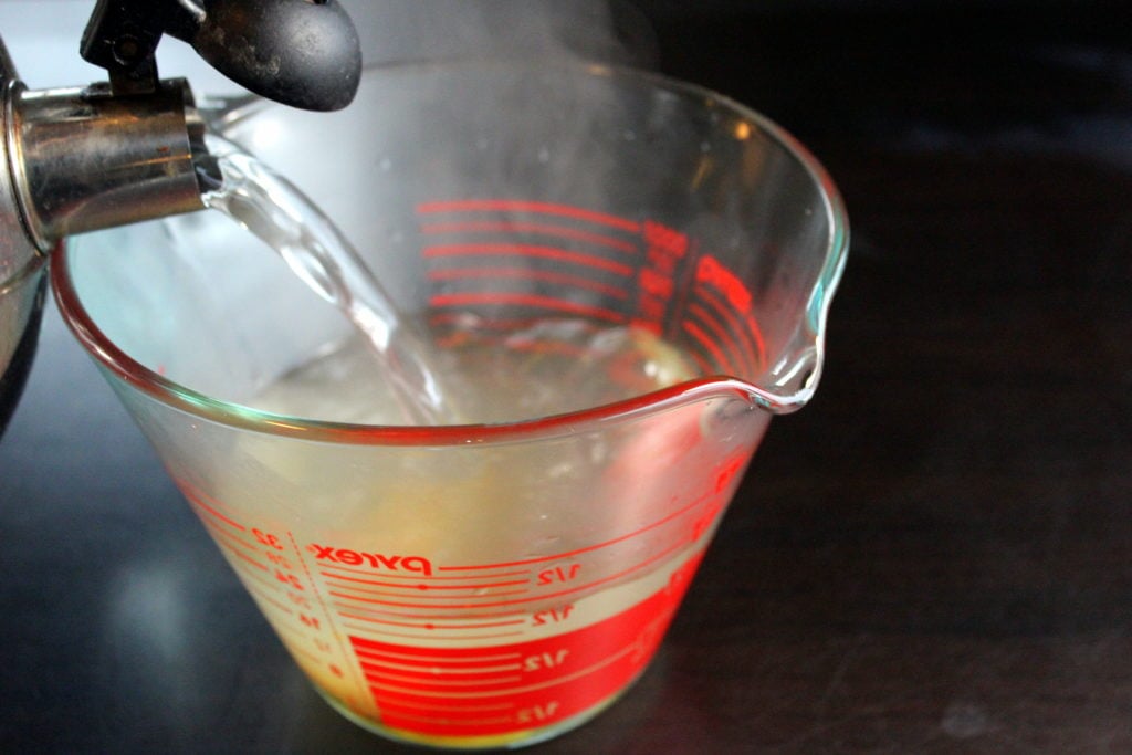 Kettle pouring boiling water in Glass Measuring Cup.