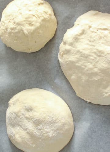 3 balls of pizza dough on parchment paper.