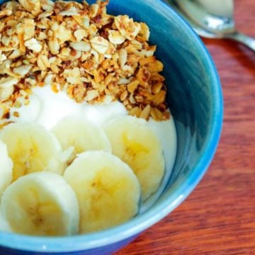 Yogurt, sliced bananas and granola in blue bowl.