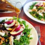 Kale salad topped with vegetables, chicken and apples on white plate.