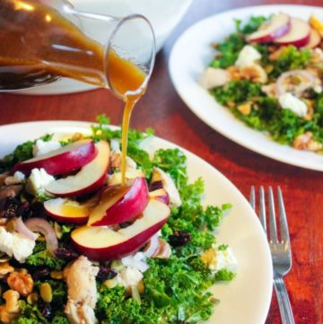 Kale salad topped with vegetables, chicken and apples on white plate.