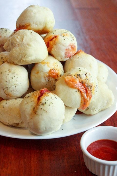 White plate piled with homemade pizza pockets and a small dish of red sauce on a brown table.