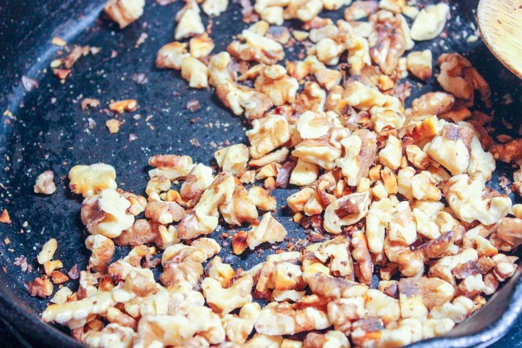 Walnuts toasting inside cast iron frying pan.