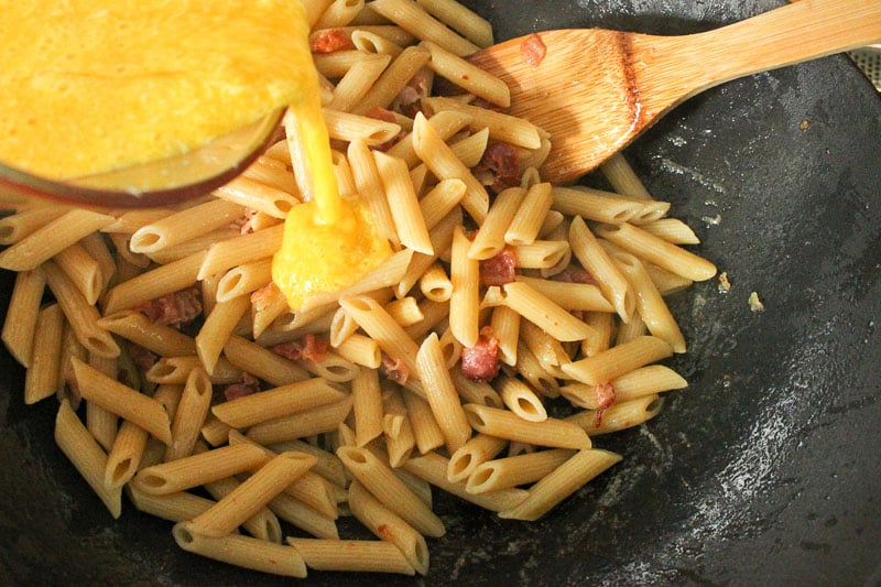Egg and Parmesan Cheese Mixture poured onto Pasta and Bacon in Wok.