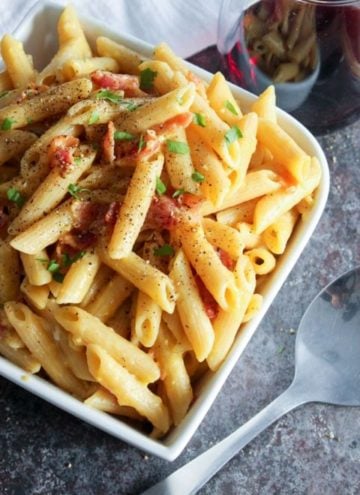 Pasta topped with bacon in white bowl.