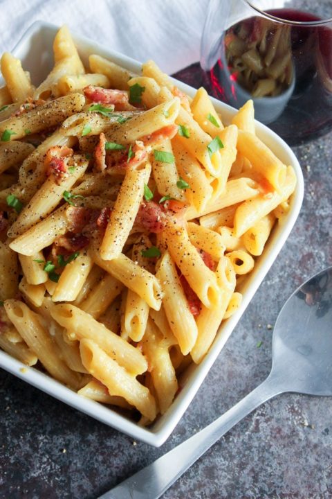 Pasta topped with bacon in white bowl.