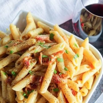 Pasta topped with bacon and green onion in white bowl.