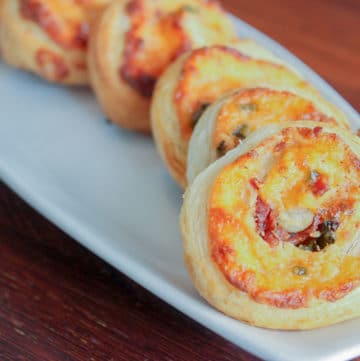 Round puff pastry appetizers on white plate.