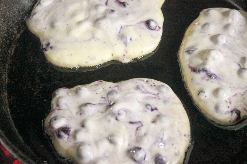 Healthy Blueberry Pancakes frying in cast iron frying pan.