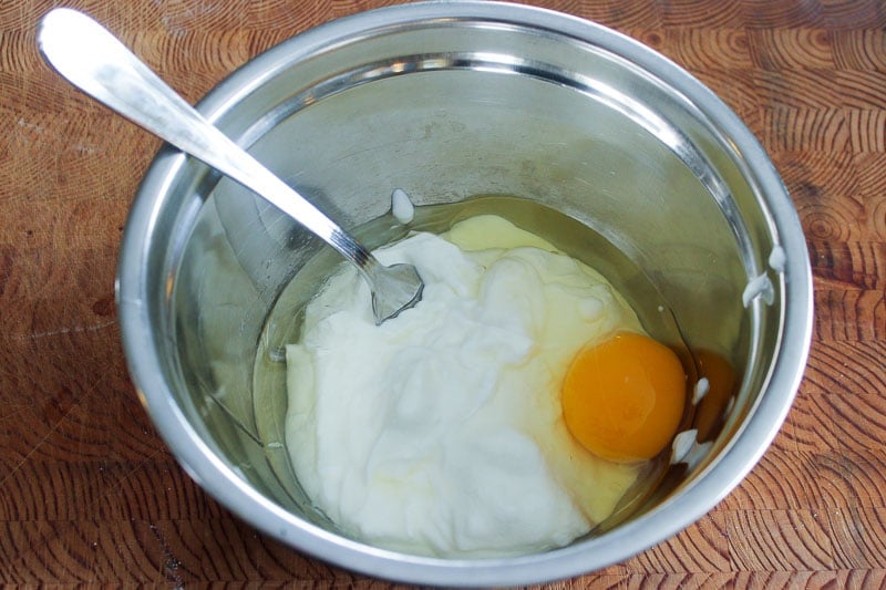 Egg, Yogurt and Oil in metal mixing bowl on wooden board.