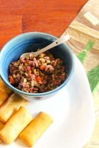 Olive tapenade in blue bowl with crackers on the side.