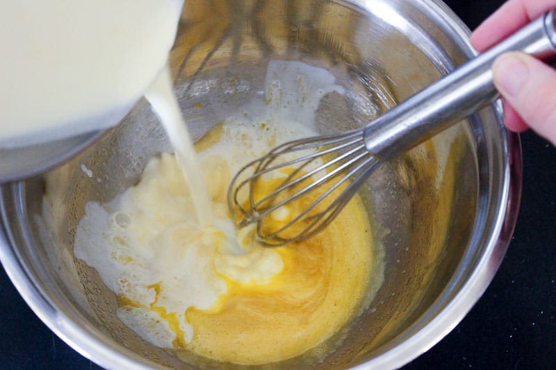Pouring whipping cream into egg mixture inside a metal mixing bowl.
