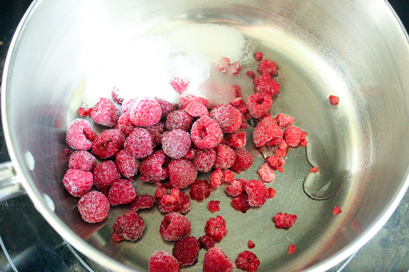 Raspberries and sugar in metal pot on stove.