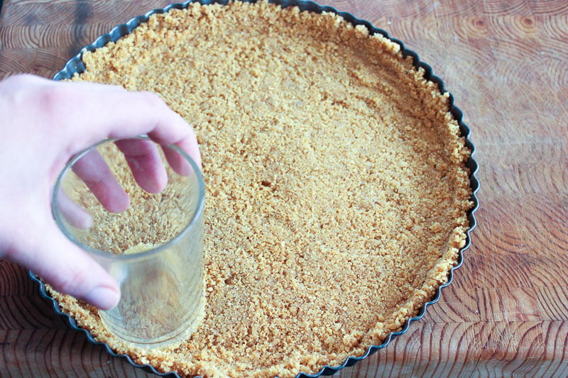 Pressing graham crumbs into tart pan with glass.