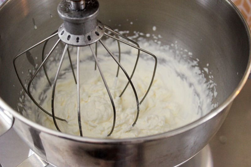 Mixed whipping cream in metal mixing bowl with stand mixer.