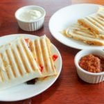 Quesadillas on white plates with small white dish of salsa.
