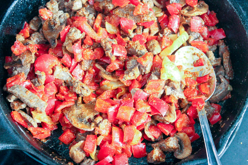 Sliced Beef and peppers frying in a cast iron pan.