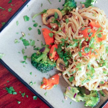 Noodles topped with vegetables and parsley on grey plate.