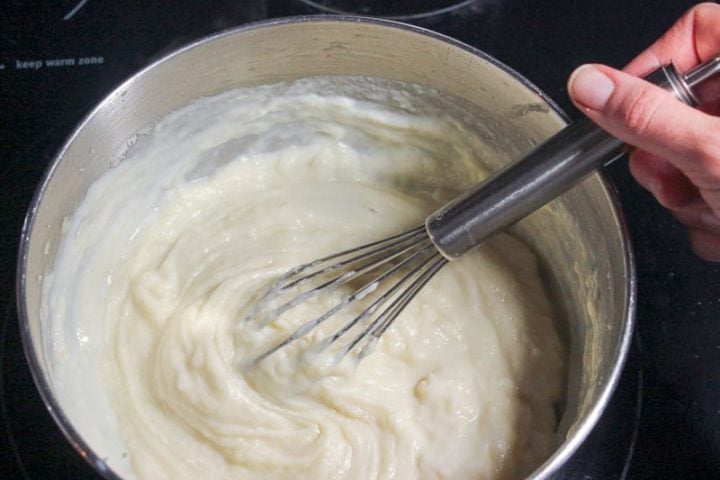 Whisking roux in metal pot on stove.