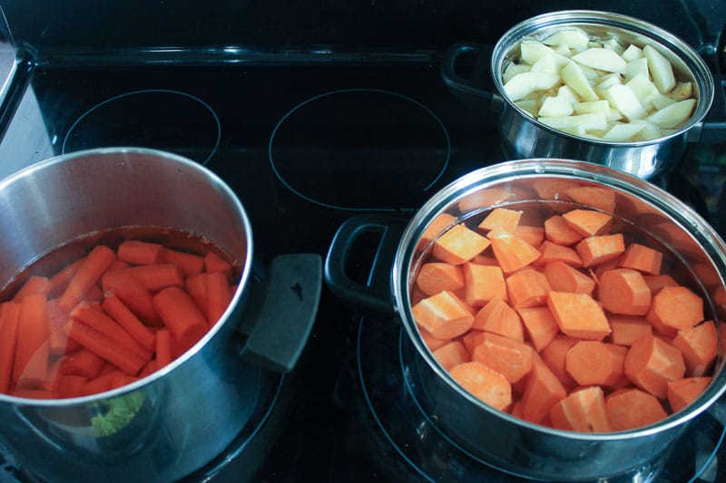 Chopped carrots, sweet potatoes and apples in pots on stove.