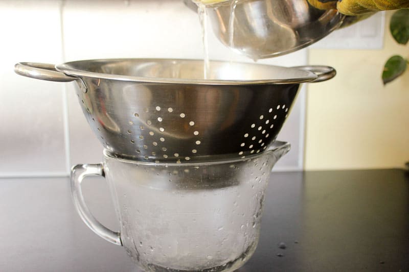 Pouring liquid through a colander into glass measuring bowl.
