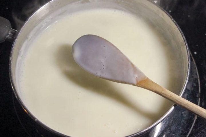 Wooden spoon in white roux mixture in metal pot.