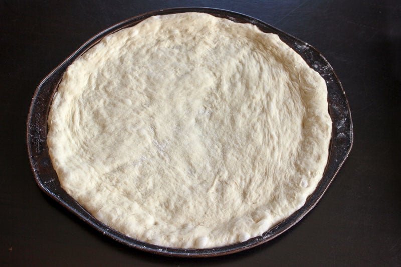 Pizza Dough on a round pizza pan on a black background.