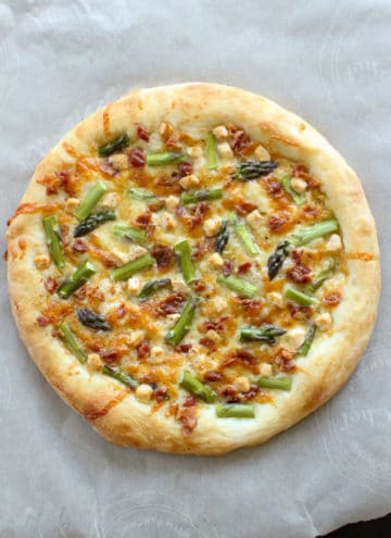 Pizza topped with bacon, asparagus and goat cheese on parchment paper.