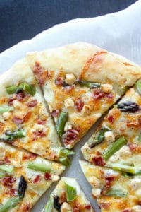 Sliced Asparagus Bacon Goat Cheese Pizza on Parchment Paper.