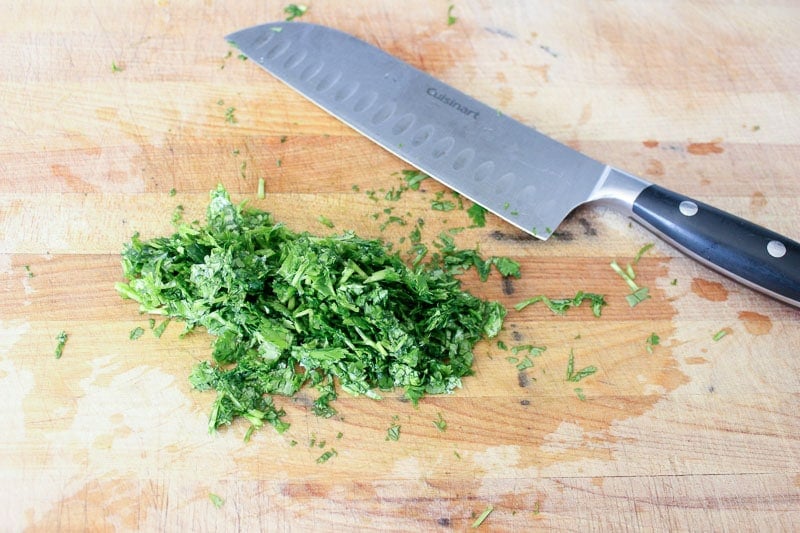 Chopped cilantro and knife on wooden board.