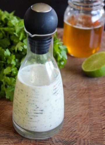 White dressing in glass jar next to honey, lime and cilantro.