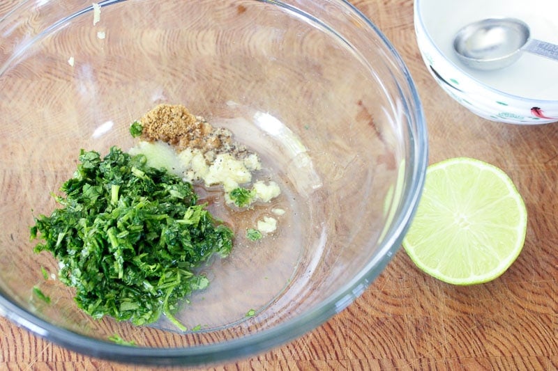 Chopped cilantro, garlic and cumin in glass mixing bowl.