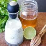 White dressing in glass jar next to honey, lime and cilantro.