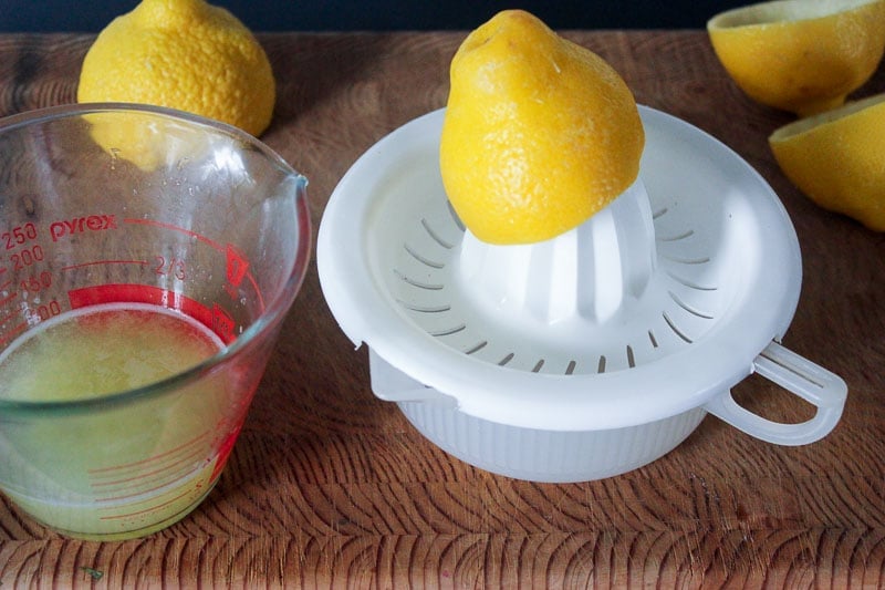 Lemon Juice in Glass Measuring Cup with Lemons and White Juice on Wooden Board.