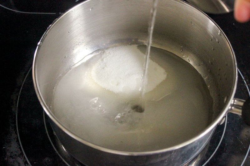 Water poured into sugar in metal pot on stove.