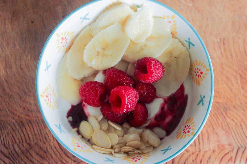 Raspberries, Sliced Bananas, Almonds and Yogurt in White Bowl.