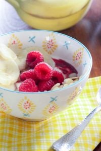 Yogur, frambuesas y rodajas de plátano en bol blanco.