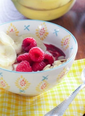 Yogurt with sliced bananas and raspberries in white bowl.