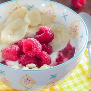 Yogurt with sliced bananas and raspberries in white bowl.