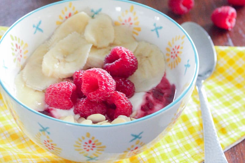 Yogurt, Sliced bananas, raspberries and almonds in white bowl.