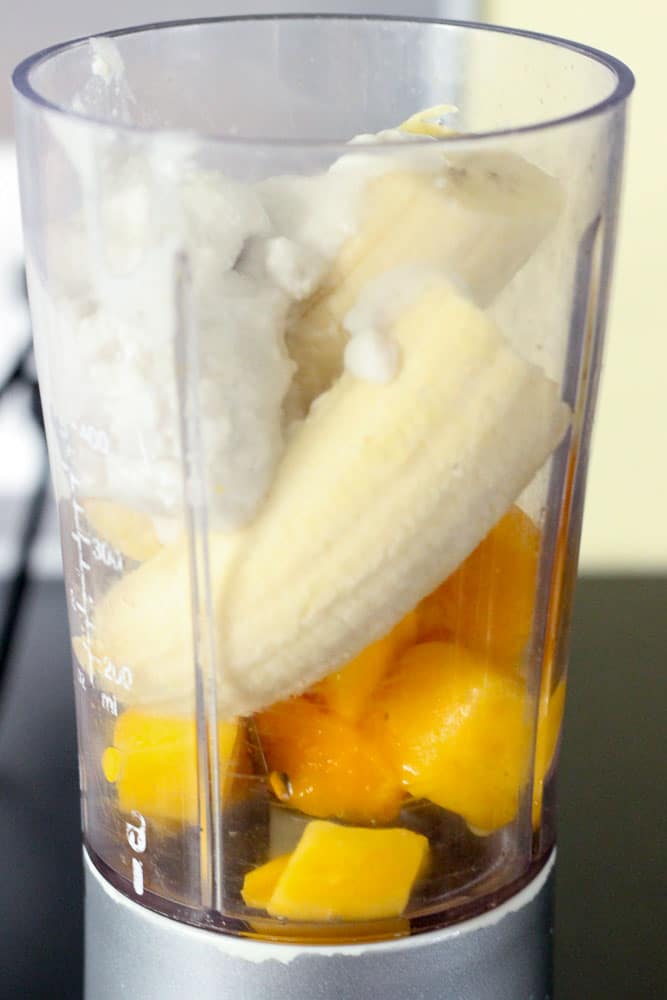 Blender containing bananas, cubes of mango and coconut milk