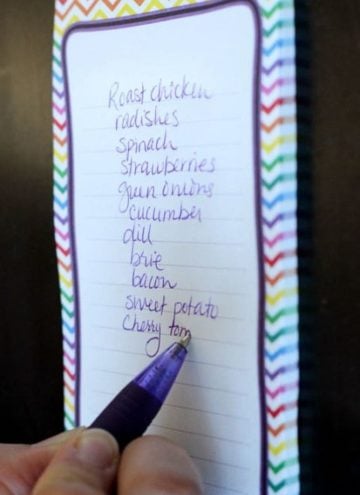 Person with purple pen writing words on a note pad.