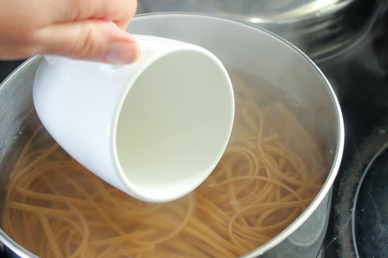 White coffee mug Getting Pasta Water from Pot on Stove.