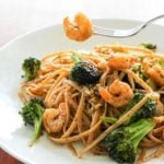 Pasta topped with shrimp and broccoli in white plate.