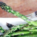 Asparagus stalk on fork and asparagus on white plate.